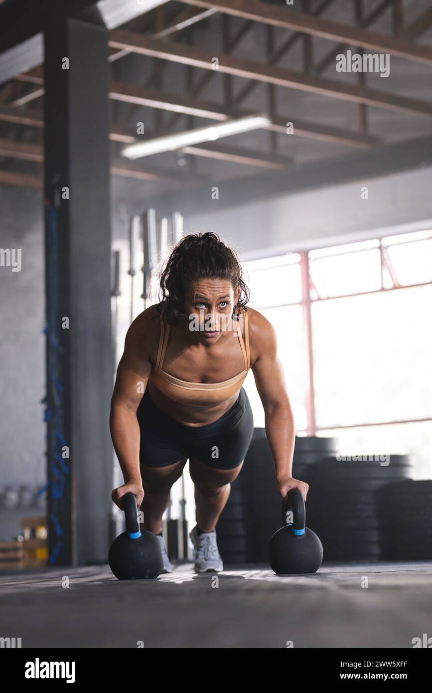 Una donna caucasica forte e in forma è impegnata in un allenamento di kettlebell in palestra Foto Stock