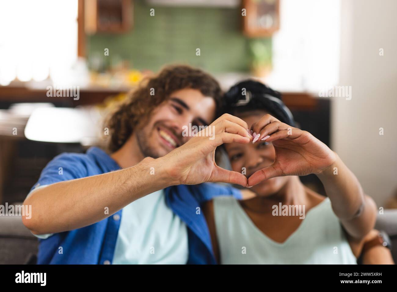 Una coppia diversificata forma il cuore con le mani a casa sul divano Foto Stock