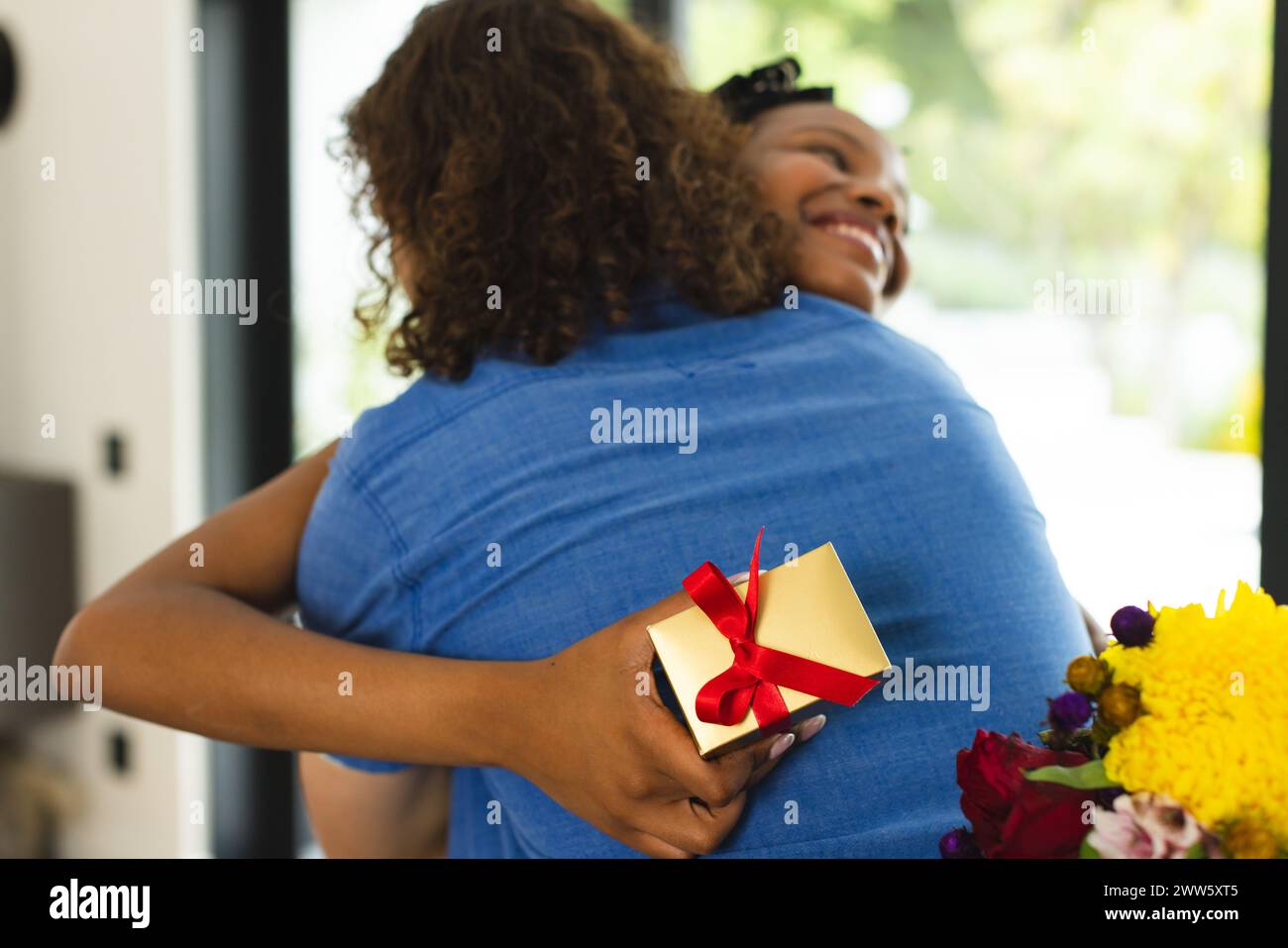 La coppia afro-americana abbraccia calorosamente, donna che tiene un dono Foto Stock