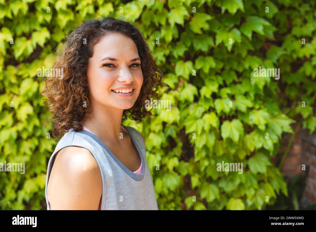 Una giovane donna caucasica sorride all'aperto, sfondo verde con spazio per le copie Foto Stock