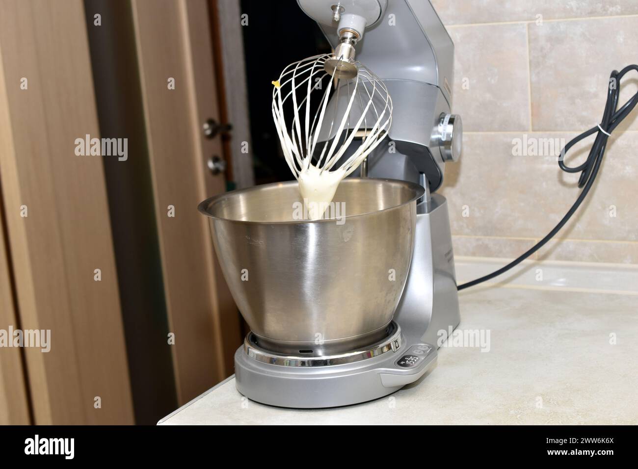 Vista laterale di un mixer da cucina con frusta e recipiente in metallo inossidabile dopo aver preparato la panna. Foto Stock