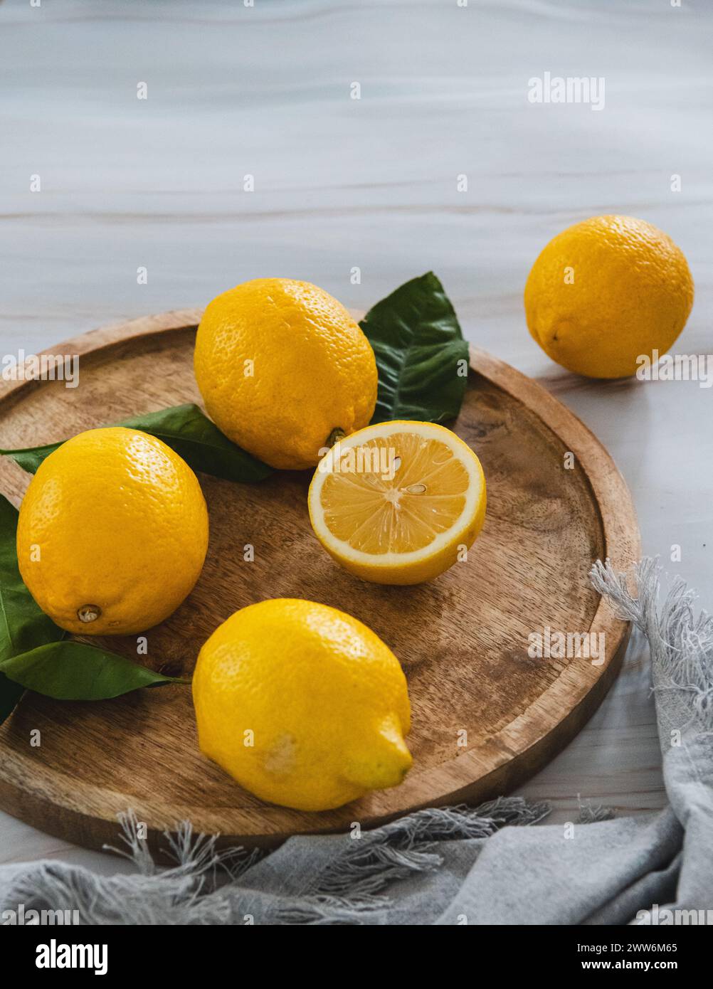 Limoni e tagliati a metà limone con foglie verdi su vassoio di legno, tovagliolo grigio e tavolo di marmo Foto Stock