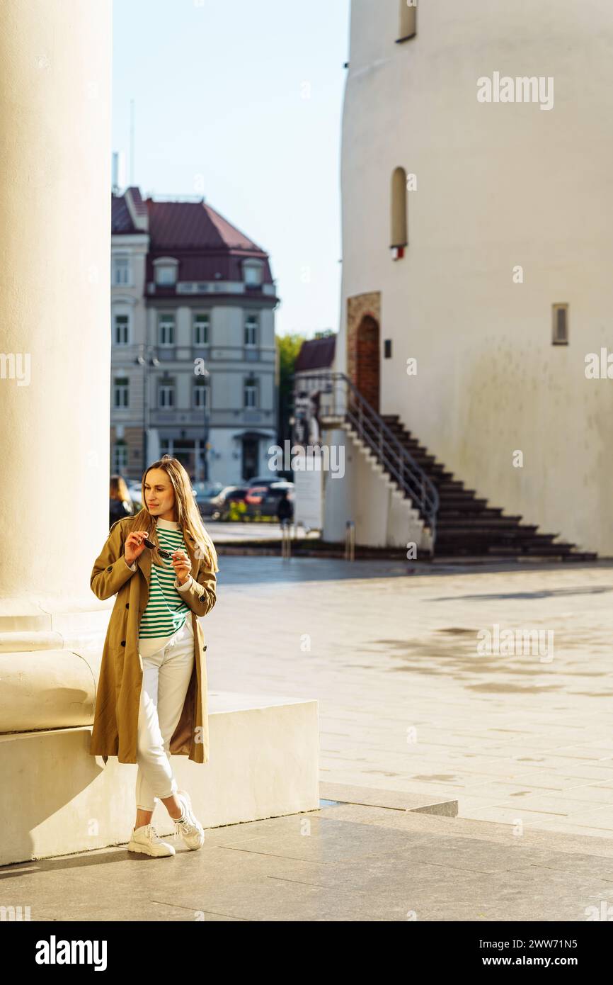 Una giovane donna attraente in abiti casual si trova nella piazza della città vicino alla colonna Foto Stock