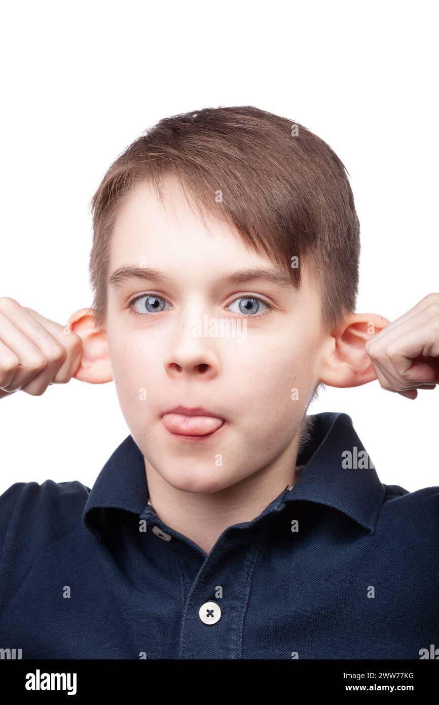 Un ragazzo che indossa una polo blu che tira le orecchie e tira fuori la lingua per creare un volto divertente. Ritratto in studio su sfondo bianco Foto Stock