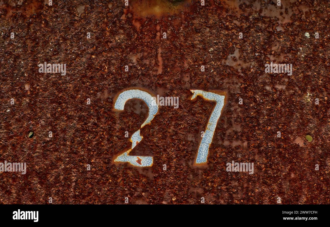 Primo piano di una vecchia piastra di metallo arrugginita con il numero 27 inciso di colore bianco Foto Stock