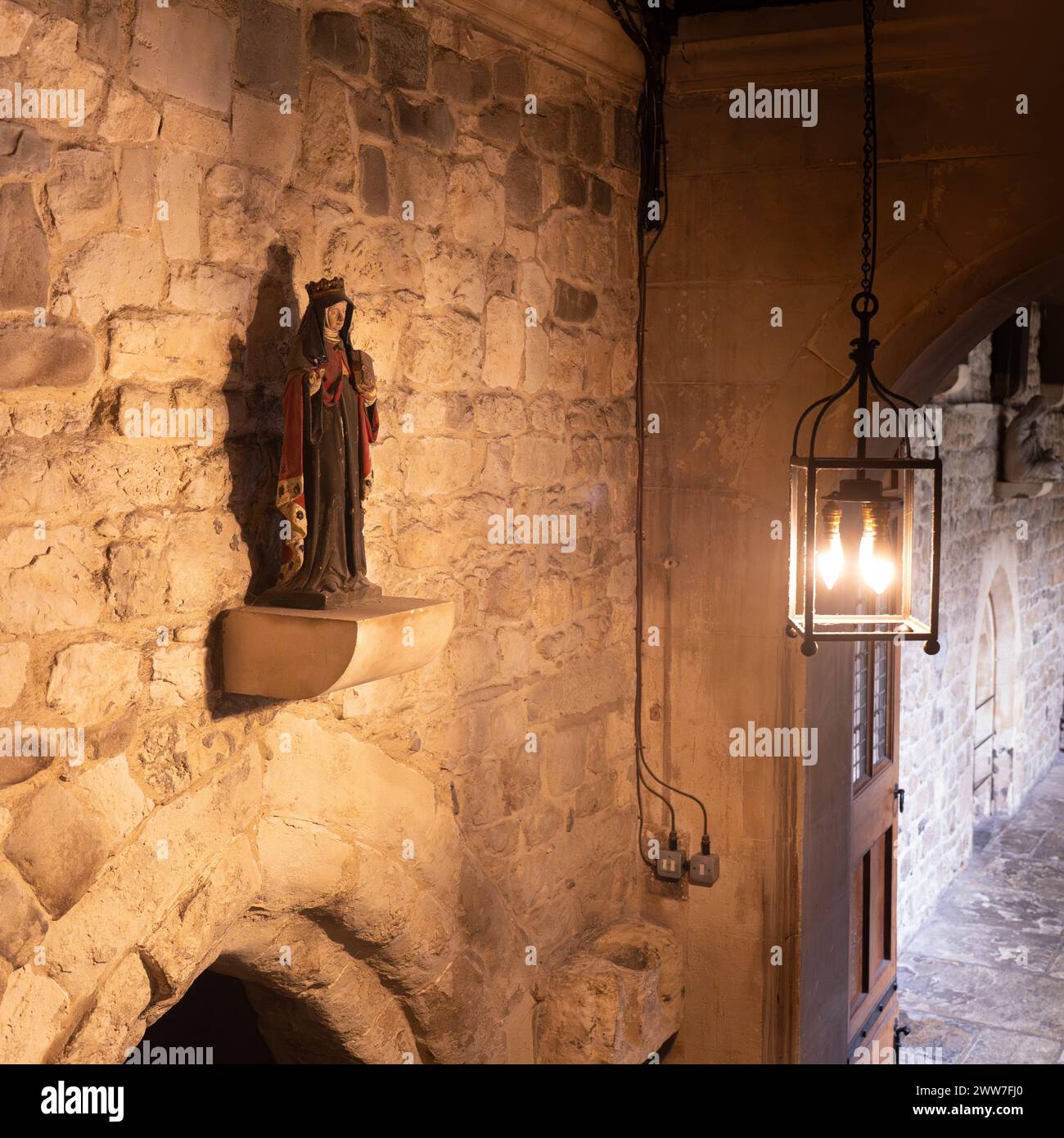 Una statua in stile medievale di un santo, annidata in un'alcova di pietra, illuminata da una luce calda Foto Stock