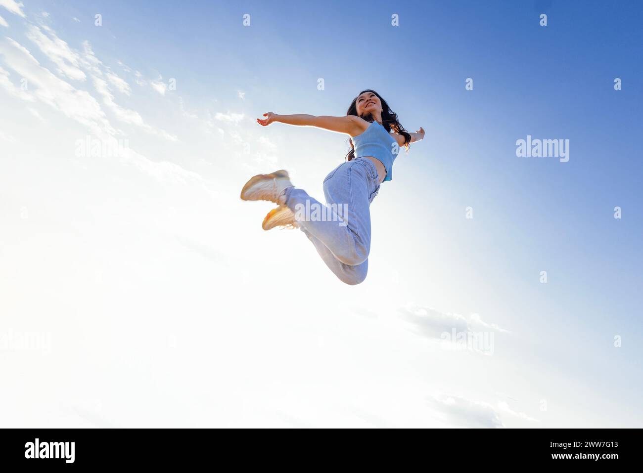 L'affascinante ragazza asiatica con i capelli delle onde lunghe in abiti casual sta saltando e ridendo all'aperto. Giovane donna coreana allegra divertirsi in natura. Bello Foto Stock