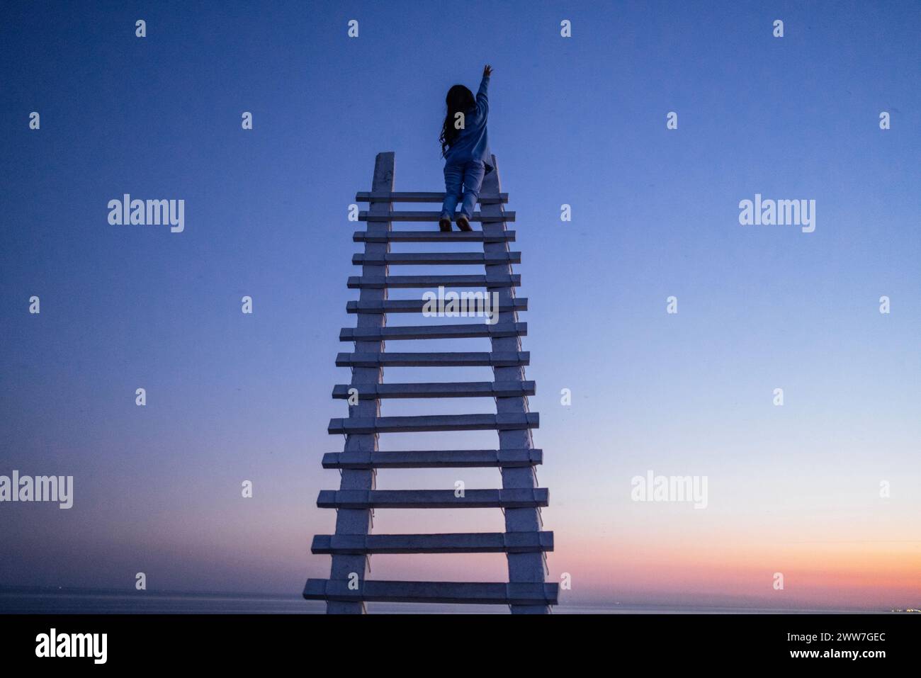 Una attraente donna asiatica sta ridendo e siede in cima ad una scala di legno all'aperto. Un'affascinante donna coreana felice ha sparso le braccia ed è Foto Stock