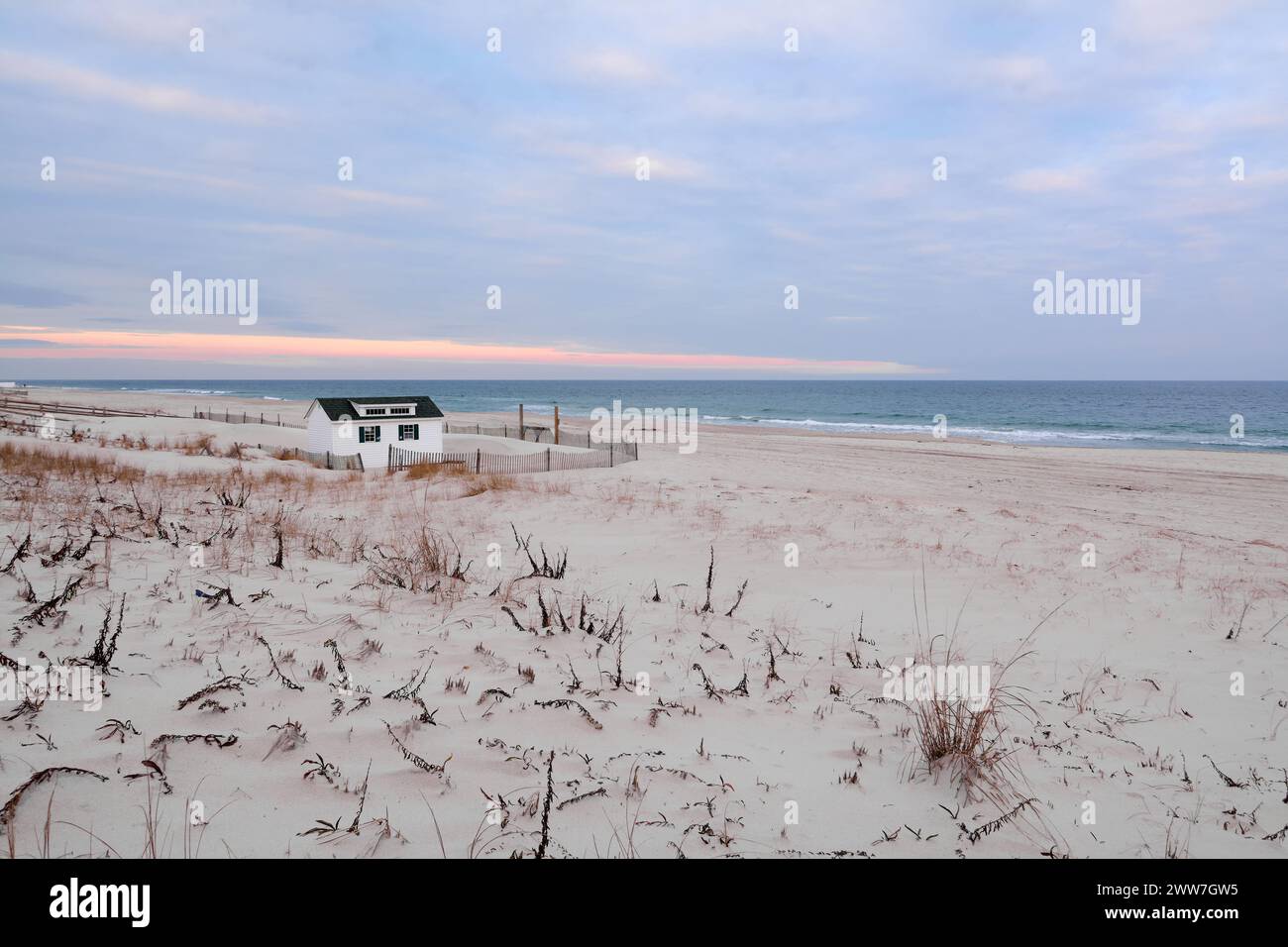 La tranquilla scena di una spiaggia all'alba, con una piccola cabina, cielo colorato e vegetazione costiera che creano un'atmosfera di pace e serenità. Foto Stock