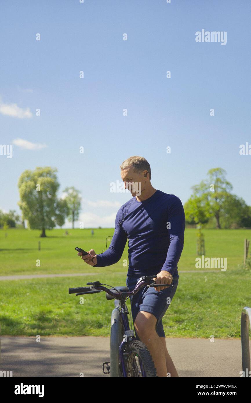 Uomo maturo nel parco con bicicletta per ascoltare musica sullo smartphone Foto Stock