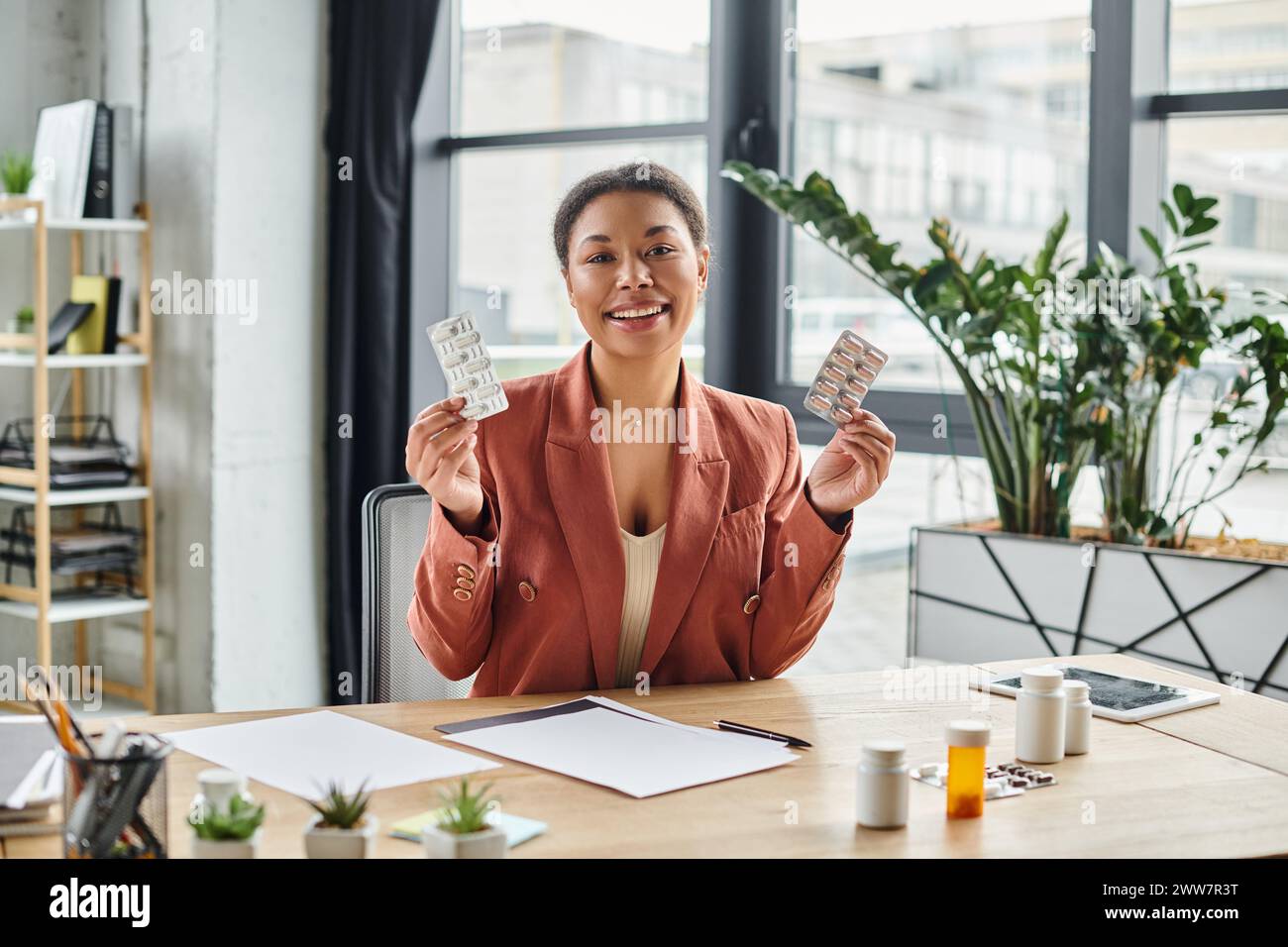 gioiosa nutrizionista afroamericana che mostra diversi farmaci mentre siede nel suo ufficio Foto Stock