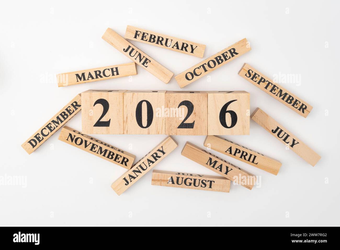 Blocchi di legno e cubetti con l'anno 2026 e i 12 mesi dell'anno sparpagliati casualmente. Isolato su sfondo bianco. Foto Stock