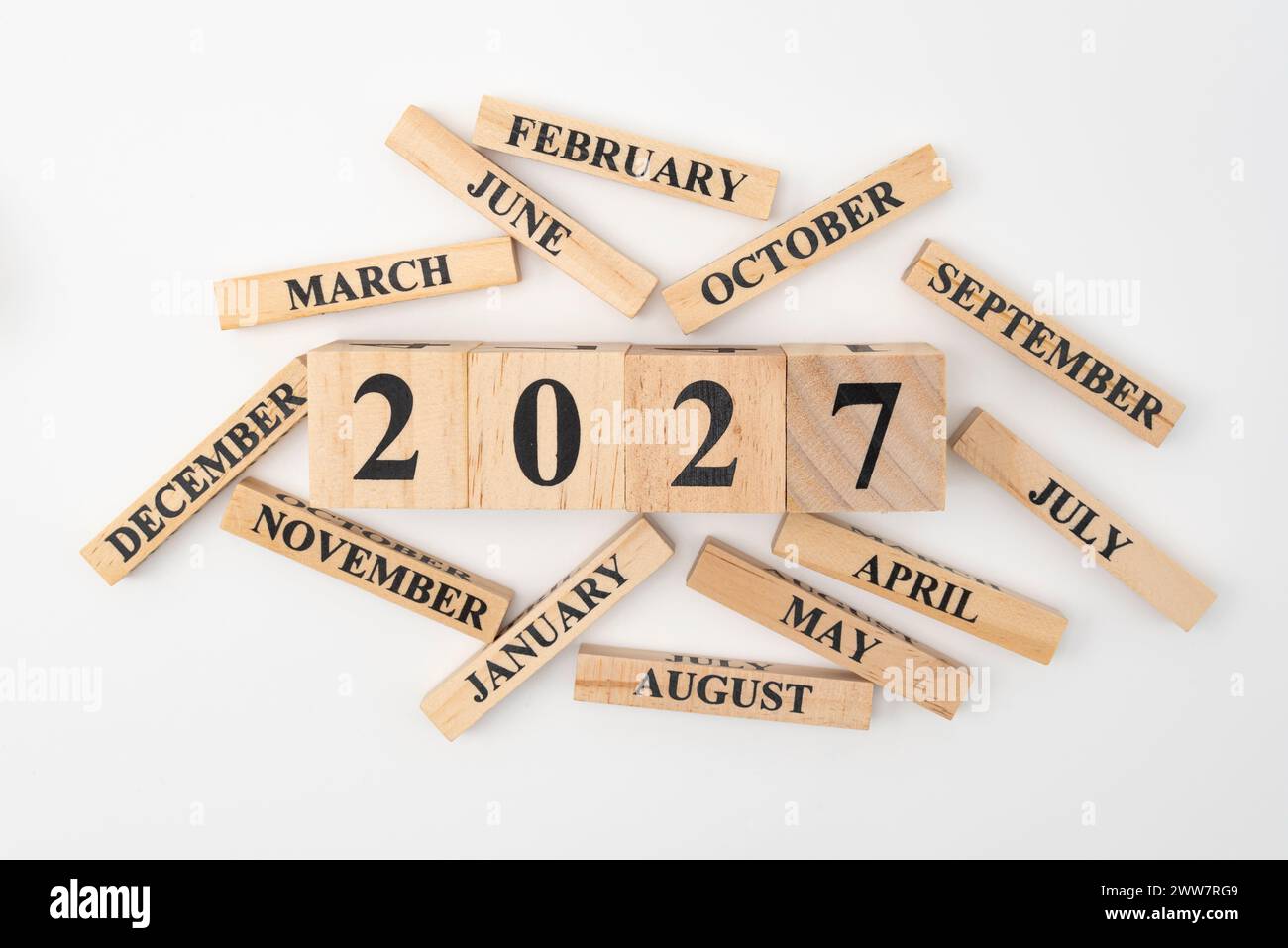 Blocchi di legno e cubetti con l'anno 2027 e i 12 mesi dell'anno sparpagliati casualmente. Isolato su sfondo bianco. Foto Stock