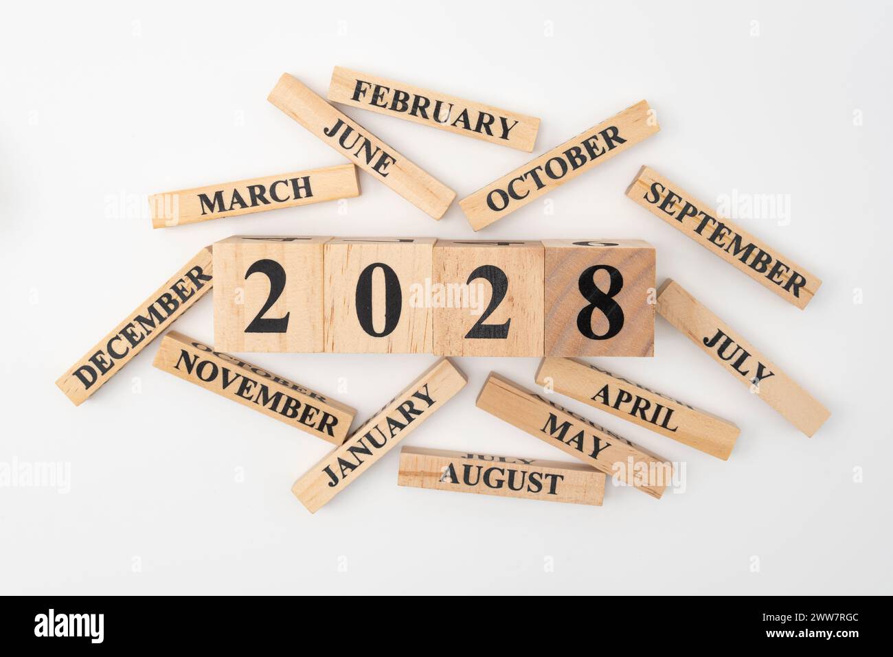 Blocchi di legno e cubetti con l'anno 2028 e i 12 mesi dell'anno sparpagliati casualmente. Isolato su sfondo bianco. Foto Stock