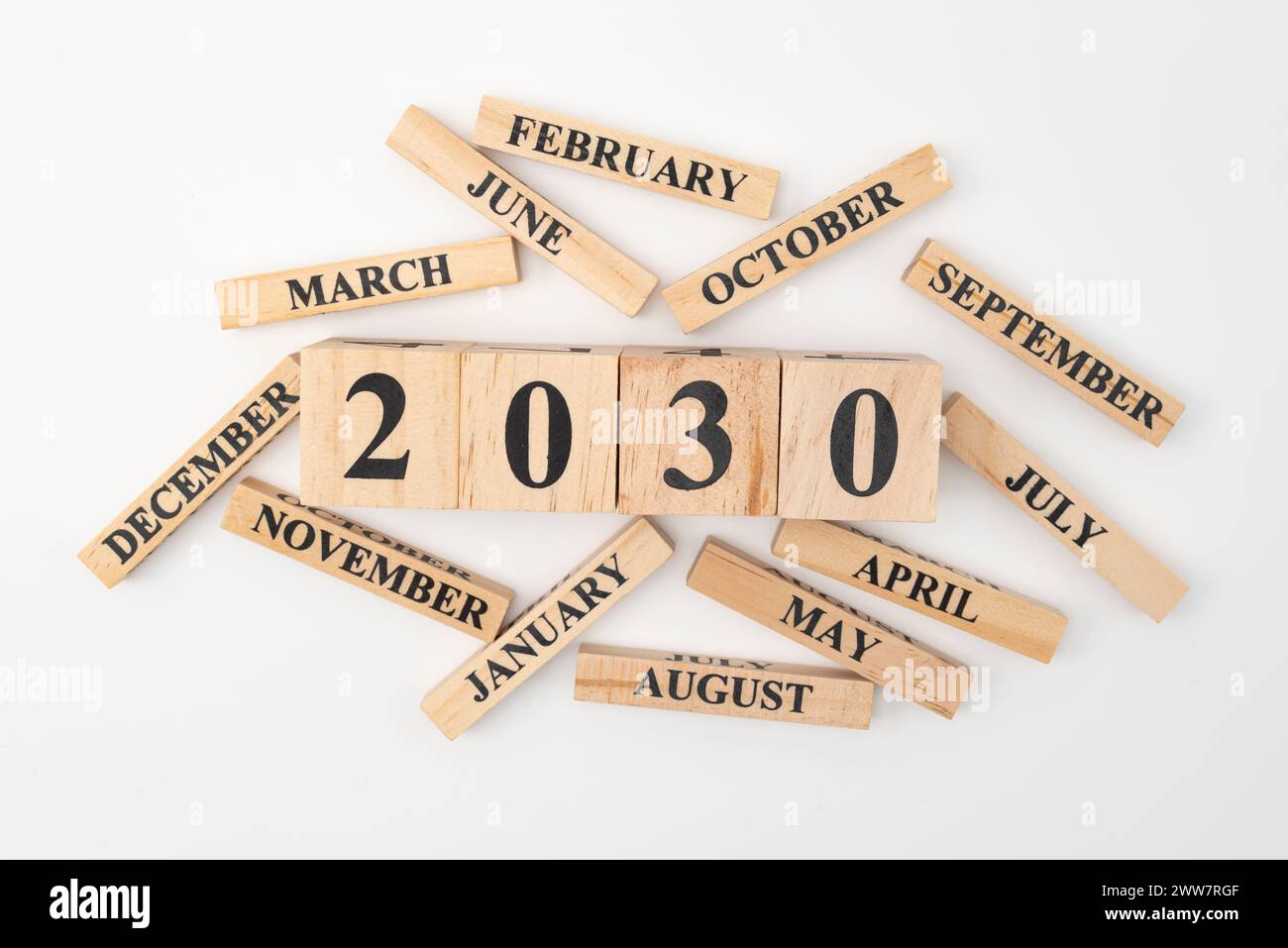 Blocchi di legno e cubetti con l'anno 2030 e i 12 mesi dell'anno sparpagliati casualmente. Isolato su sfondo bianco. Foto Stock
