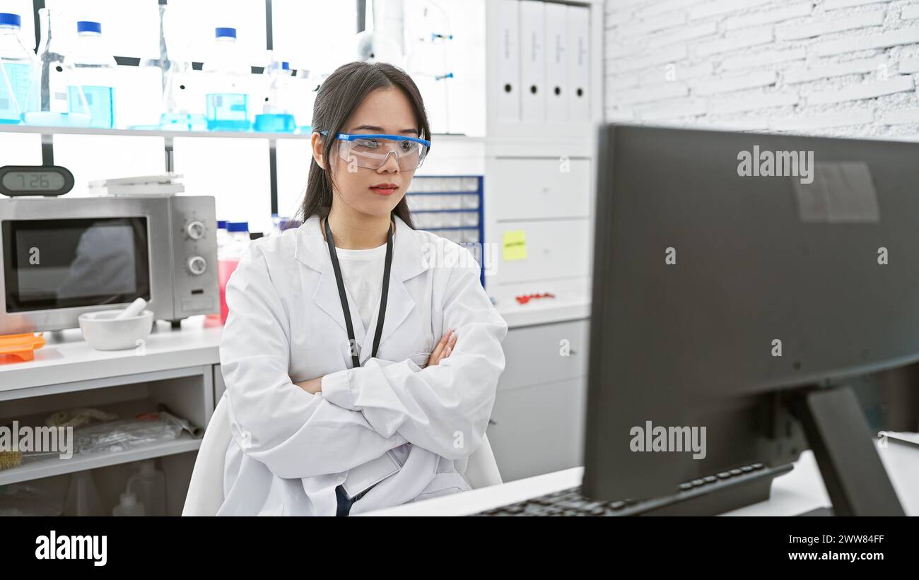Una giovane scienziata asiatica studia con fiducia i dati su un computer in un moderno laboratorio. Foto Stock