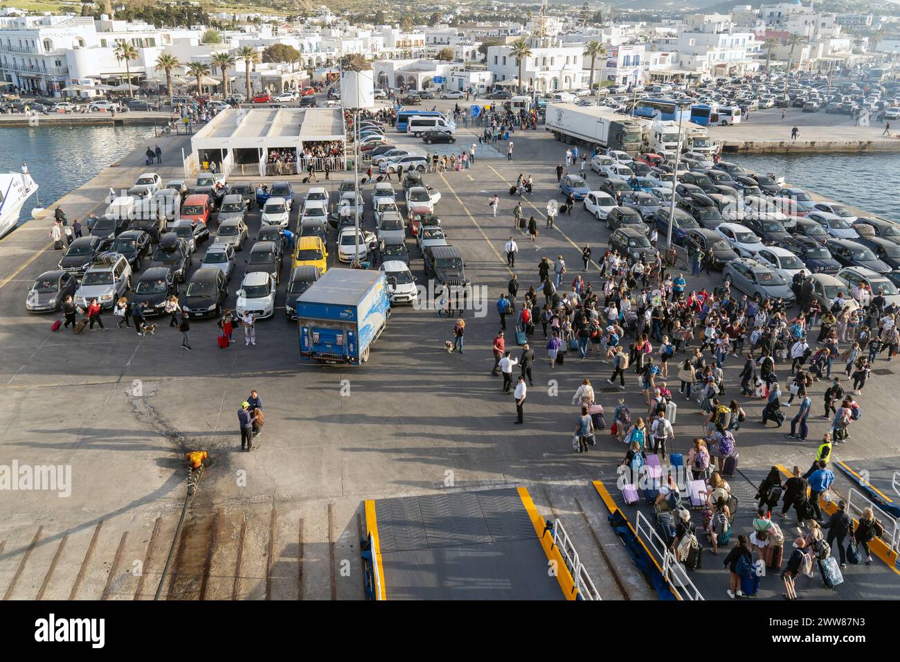 I turisti prendono il traghetto al porto di Parikia, l'isola di Paros, mentre decine di auto e camion attendono il loro turno per salire a bordo del traghetto. Foto Stock