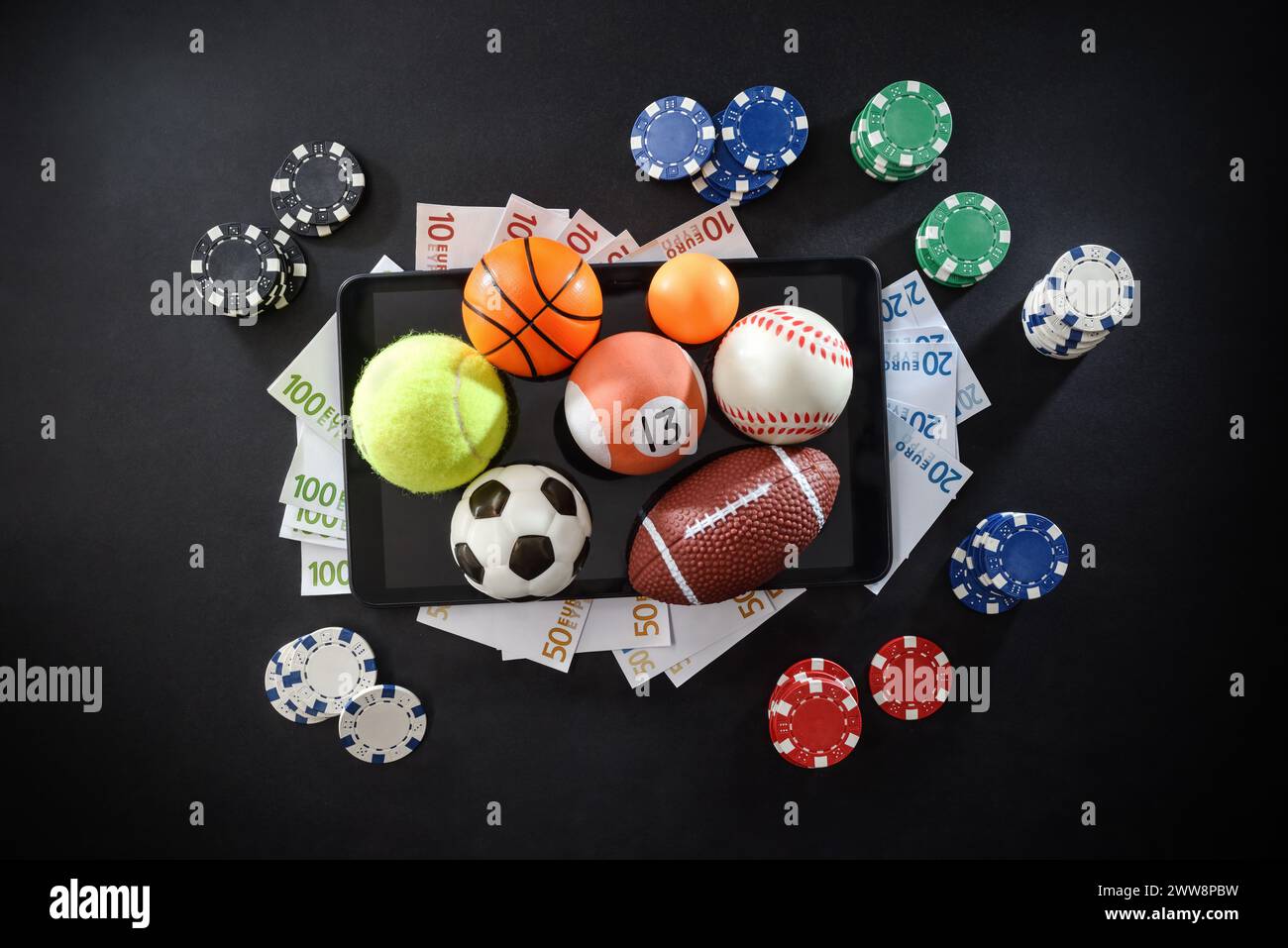 Concetto di scommesse sportive online con palloni sportivi, denaro e chip su dispositivi mobili isolati al centro su sfondo scuro. Vista dall'alto. Foto Stock