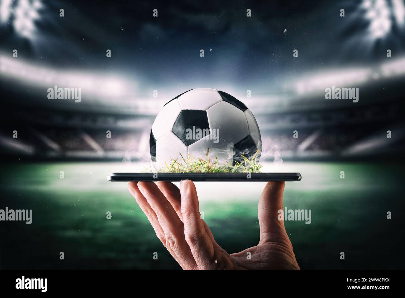 Concetto di trasmissione online in diretta del campionato di calcio con la mano che tiene in mano un telefono cellulare con palla e stadio di calcio sullo sfondo. Foto Stock