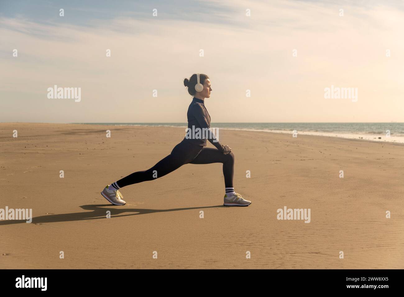 Donna sportiva che fa esercizi di riscaldamento per lo stretching delle gambe sulla spiaggia al sole Foto Stock
