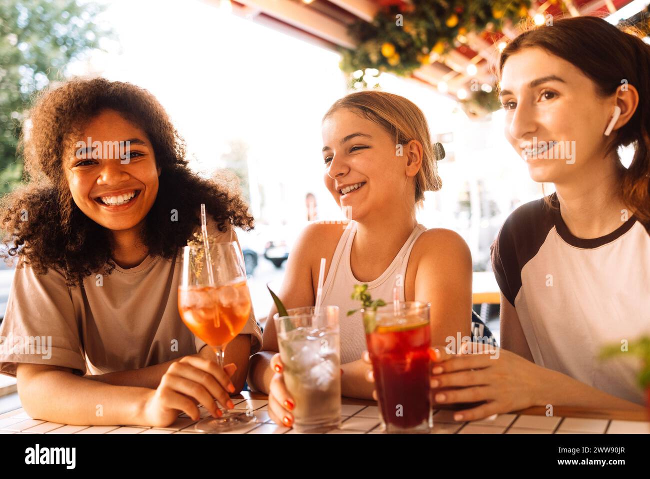 Primo piano di tre affascinanti ragazze che bevono cocktail ghiacciati in un bar. Bicchieri con deliziose bevande alla frutta e cubetti di ghiaccio. Gli amici sorridenti si rilassano e il dottor Foto Stock