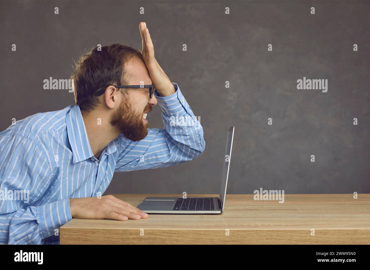 L'uomo fa un errore stupido mentre usa il suo computer e si schiaffia in faccia Foto Stock
