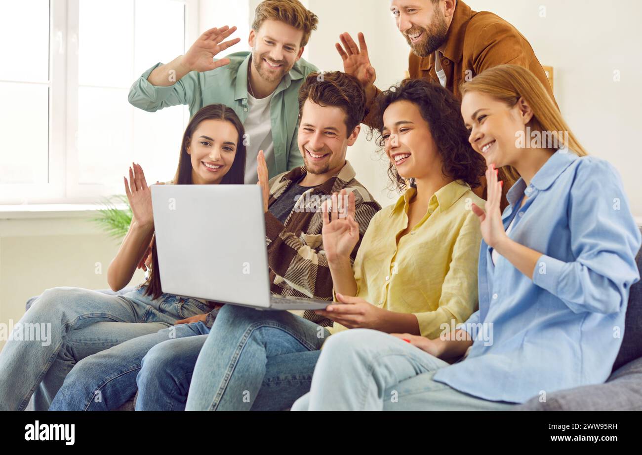 Amici allegri e felici che si divertono a videochiamare sul computer portatile seduto sul divano a casa. Foto Stock
