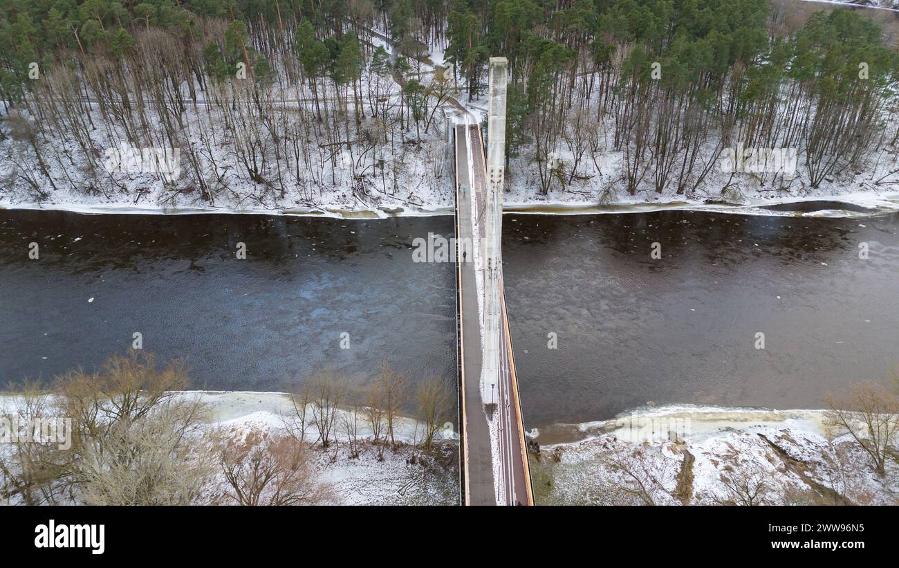 Fotografia con drone di un ponte pedonale che attraversa il fiume dalla città al parco pubblico durante il giorno nuvoloso d'inverno Foto Stock
