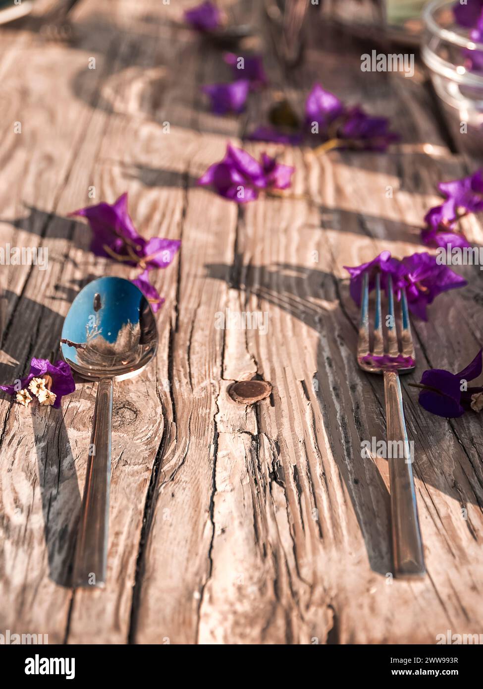 un mix romantico e moderno al posto di un ristorante con petali bounganville freschi che incorniciano un antico tavolo in legno Foto Stock