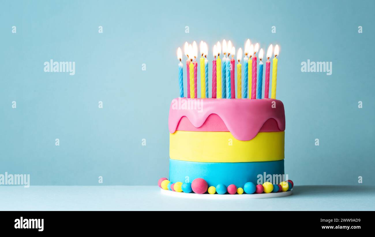 Colorata torta di compleanno con tante candele di compleanno e glassa gocciolante su sfondo blu Foto Stock