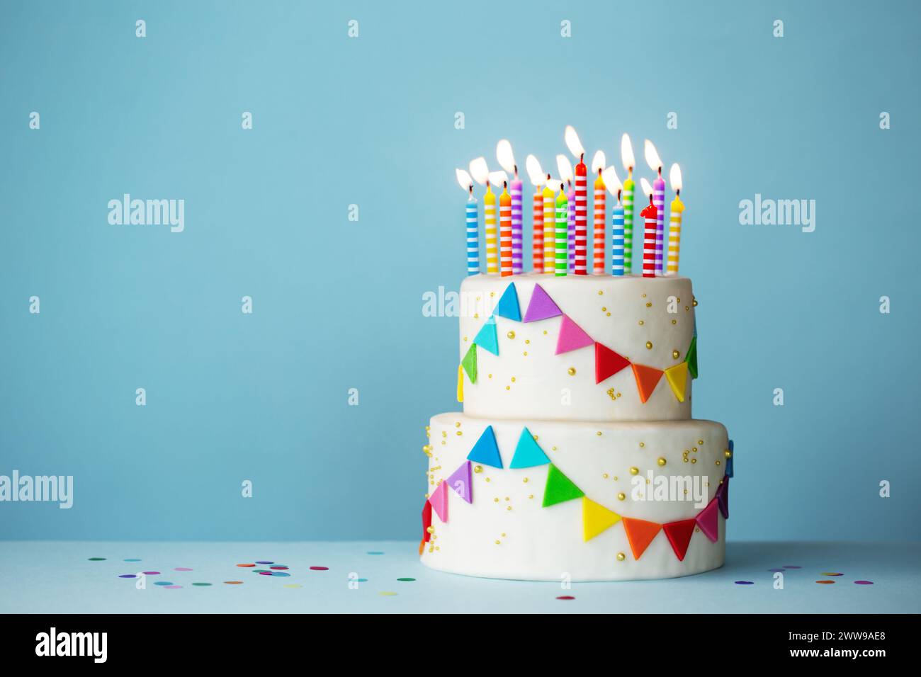 Torta di compleanno a più piani con coloratissimi mazzetti di festa e candele di compleanno su sfondo blu Foto Stock