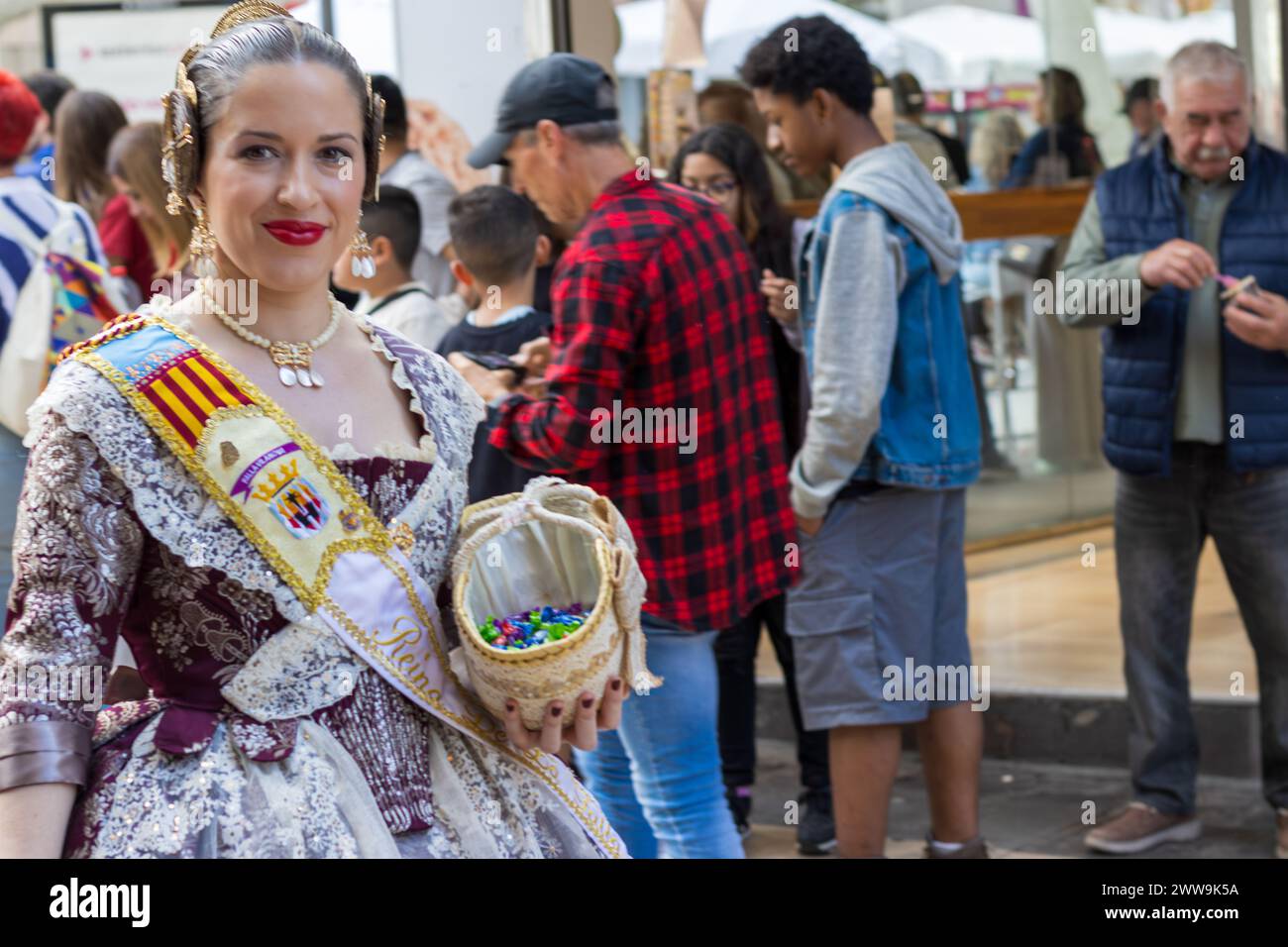 Tradizionale costume del Festival Fallas tra una folla a Gandia, Spagna. Una donna con un abbigliamento vivace si distingue, riflettendo il patrimonio culturale di Valencia Foto Stock