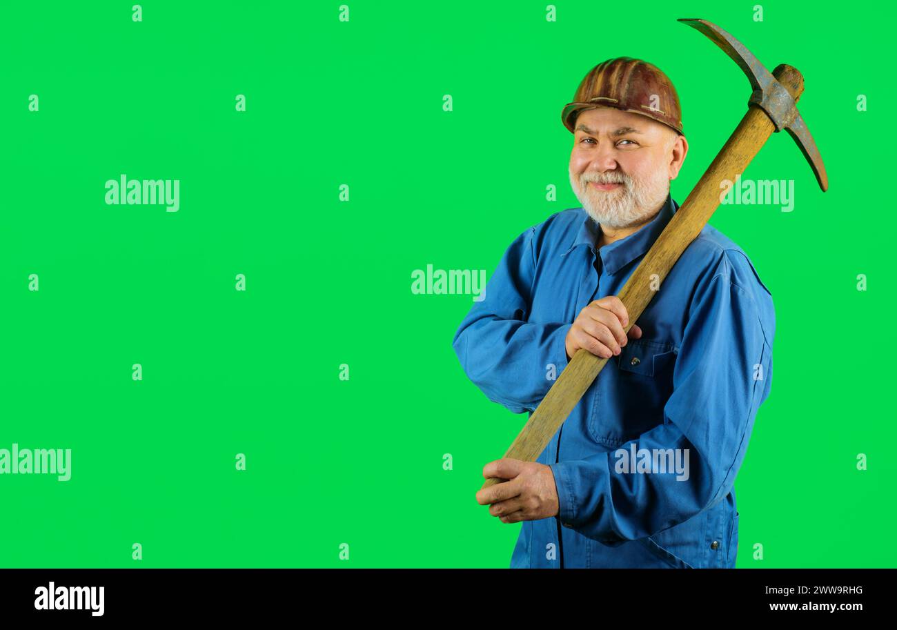 Minatore sorridente in uniforme con piccone. Lavori di costruzione e costruzione. Operaio edile con barba o artigiano in elmetto con piccone. Maschio Foto Stock