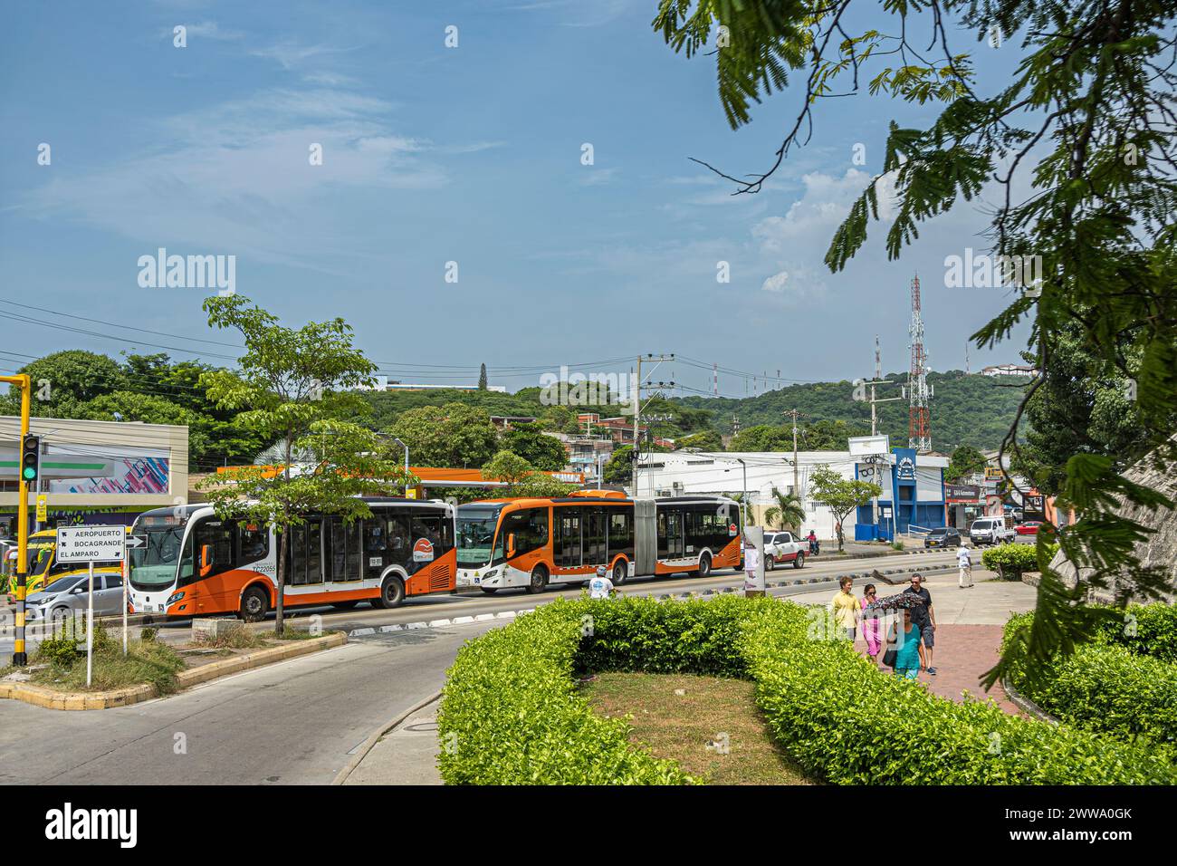 Cartagena, Colombia - 25 luglio 2023: Trasporti pubblici, 2 tipi di autobus pubblici arancioni su strade trafficate sotto il paesaggio blu e verde del verde Foto Stock