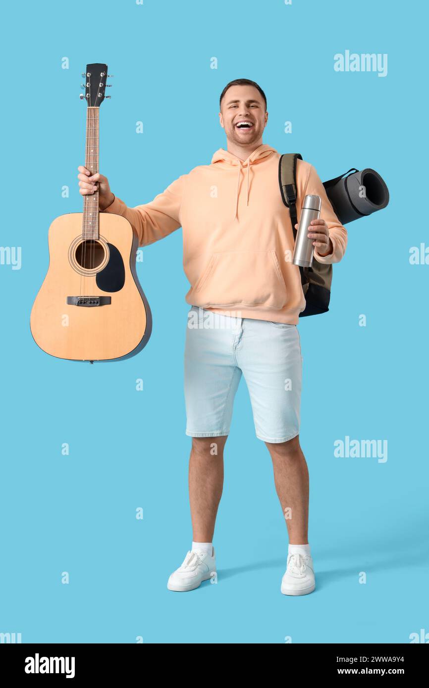 Turista maschile con zaino, thermos e chitarra su sfondo blu Foto Stock