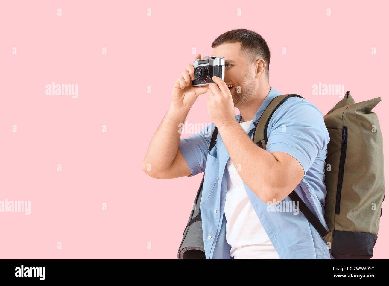 Turista maschile con zaino e macchina fotografica che scatta foto di qualcosa su sfondo rosa Foto Stock