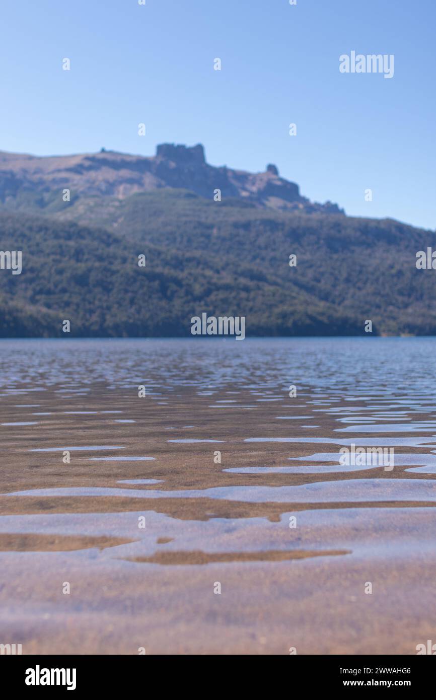Vista verticale, acqua di lago marrone ondulata sul fondo e montagne lontane piene di foresta verde scuro nel Lago Falkner, Argentina Foto Stock