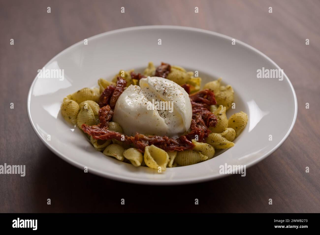 Pesto conchiglie con pomodori secchi e burrata servito in piatto bianco, poco profondo Foto Stock