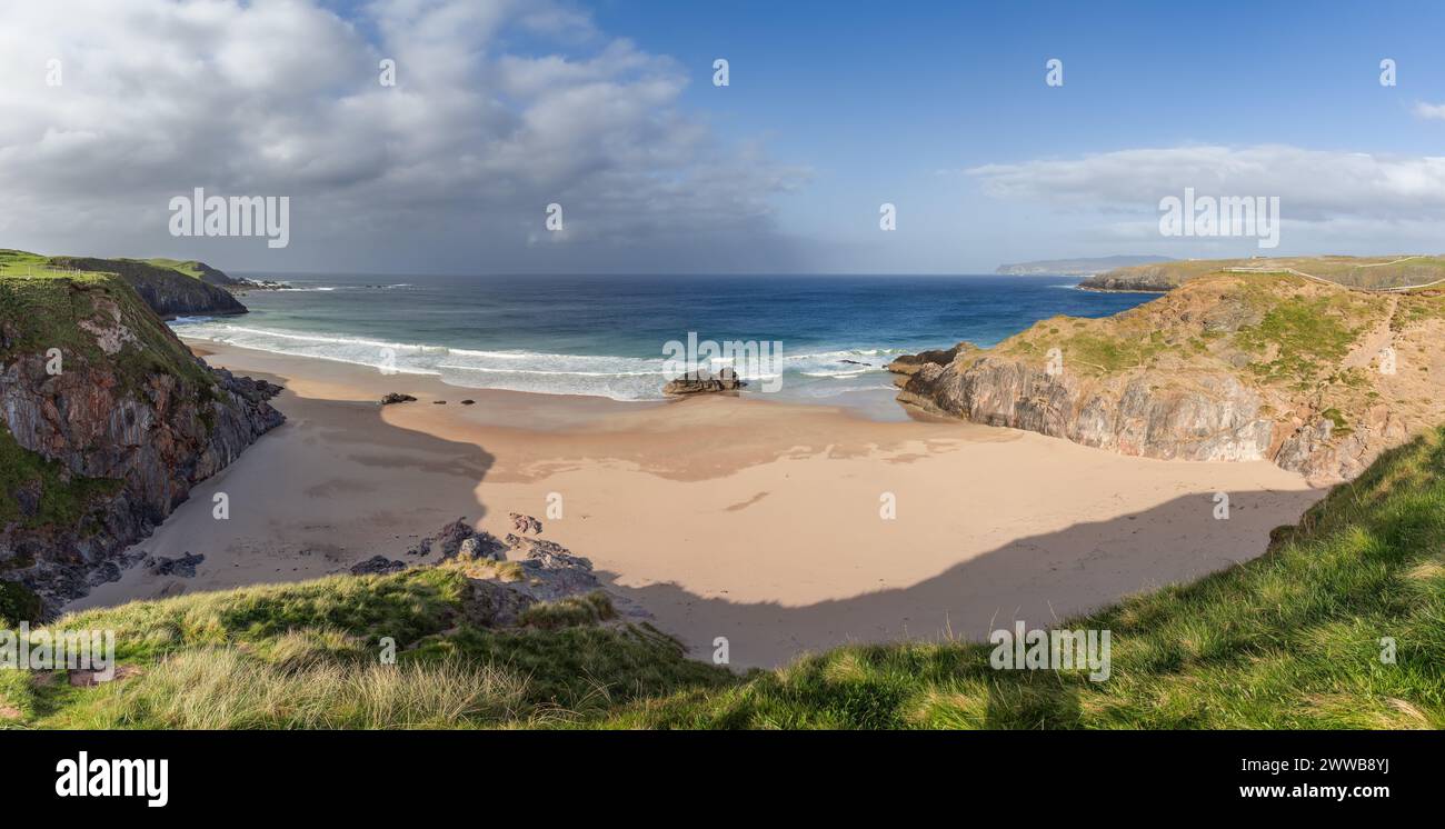 Vista panoramica di Durness Beach in Scozia, con l'ampia spiaggia di sabbia annidata tra aspre scogliere, sotto un cielo dinamico dove la luce del sole Foto Stock