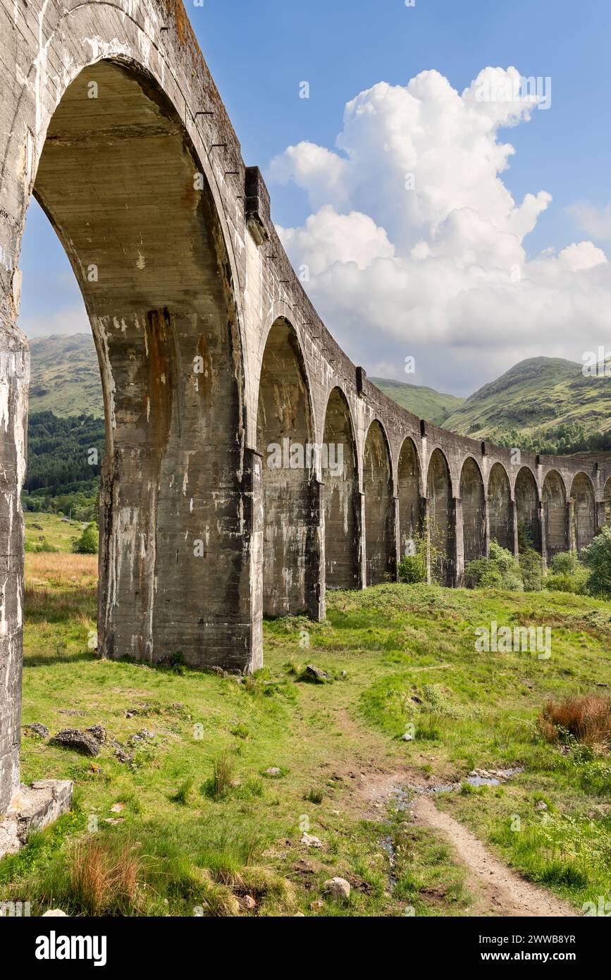 Ripresa verticale del viadotto Glenfinnan con i suoi imponenti archi che tagliano una figura impressionante contro le colline ondulate delle Highland e un cielo dinamico Foto Stock