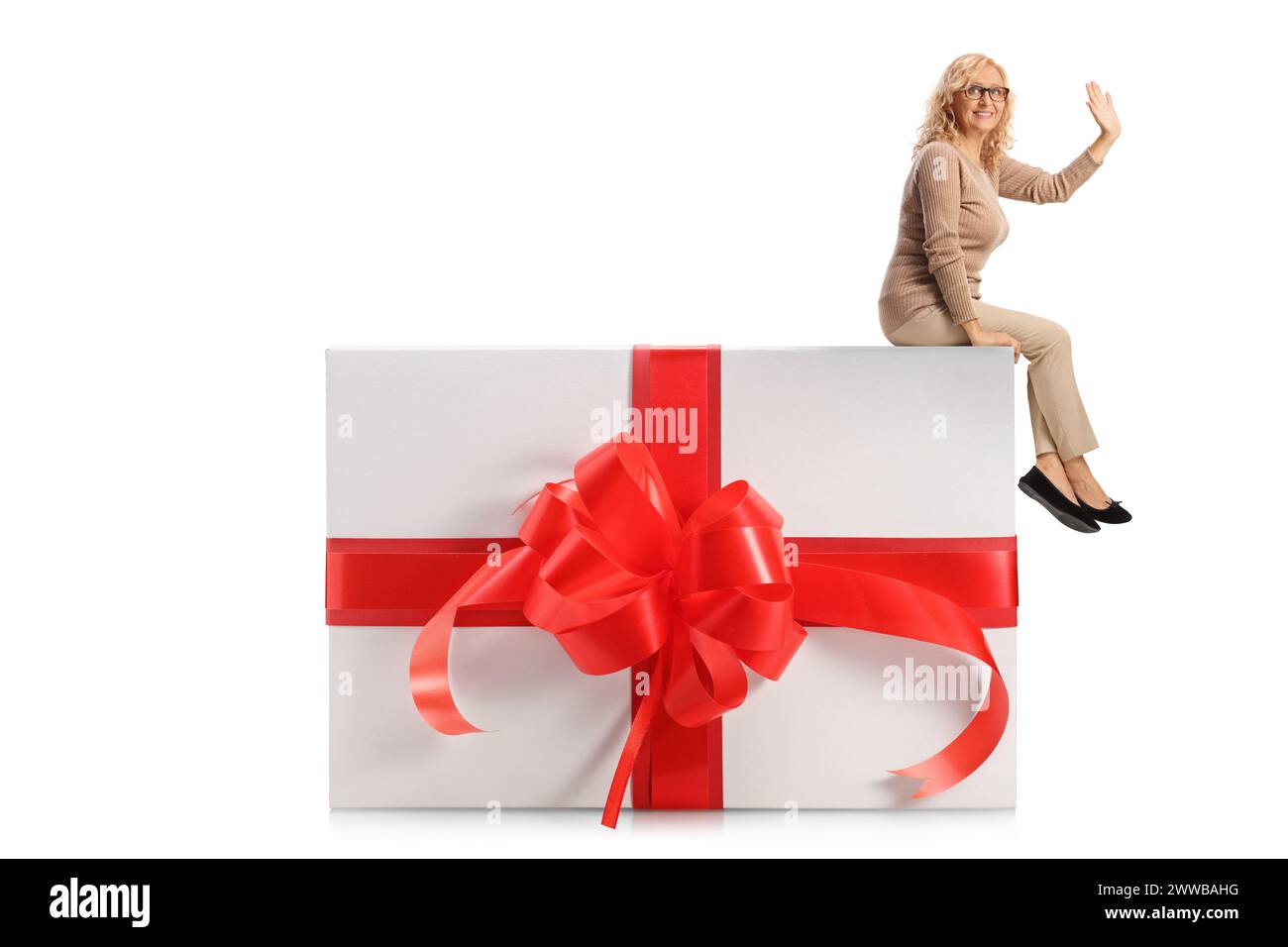 Donna informale di mezza età seduta su una grande confezione regalo e che ondeggia isolata su sfondo bianco Foto Stock