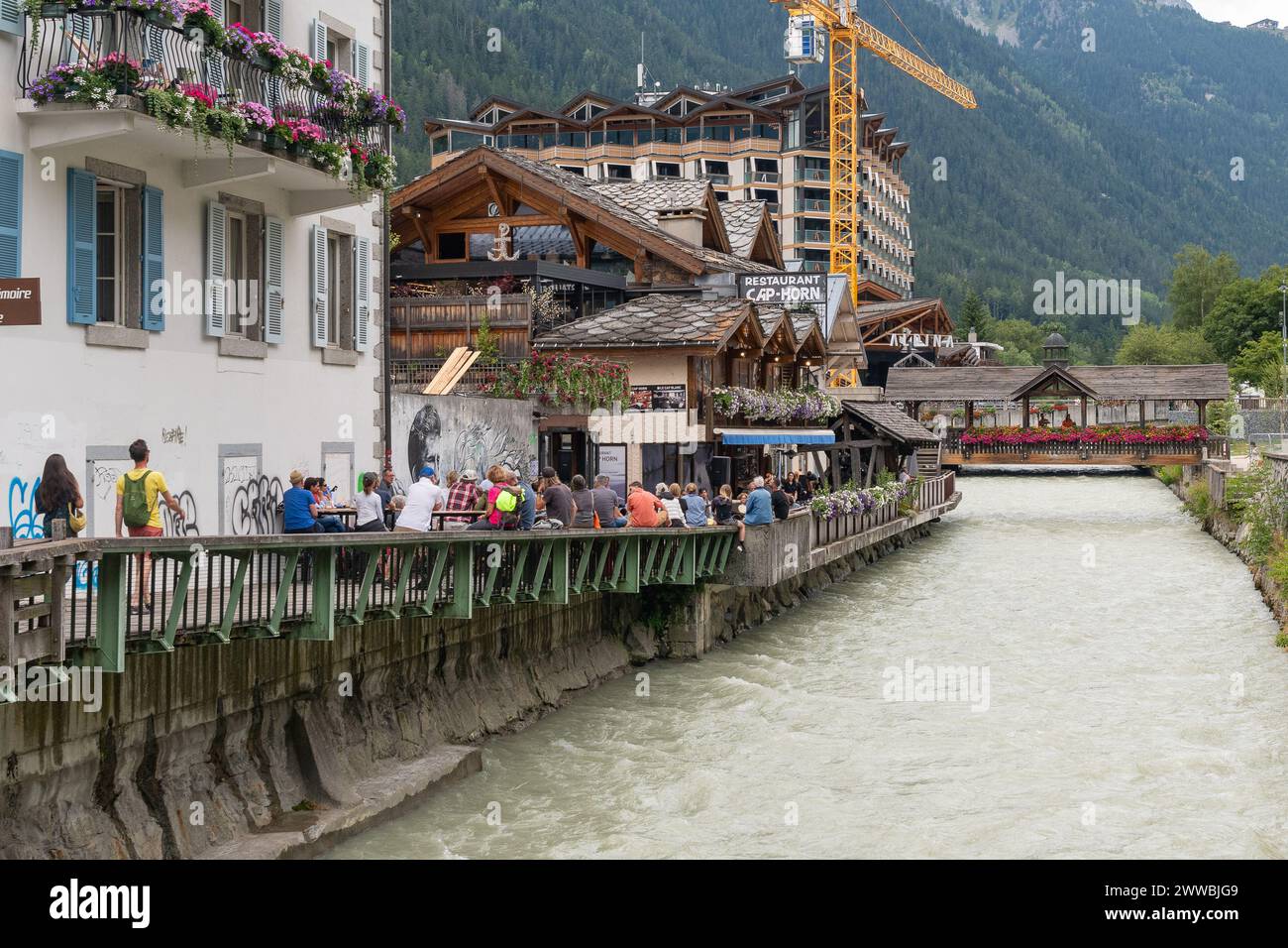 Folla di persone in un caffè all'aperto con musica dal vivo che si affaccia sull'Arve durante l'happy hour estivo, Chamonix, Haute Savoie, Francia Foto Stock