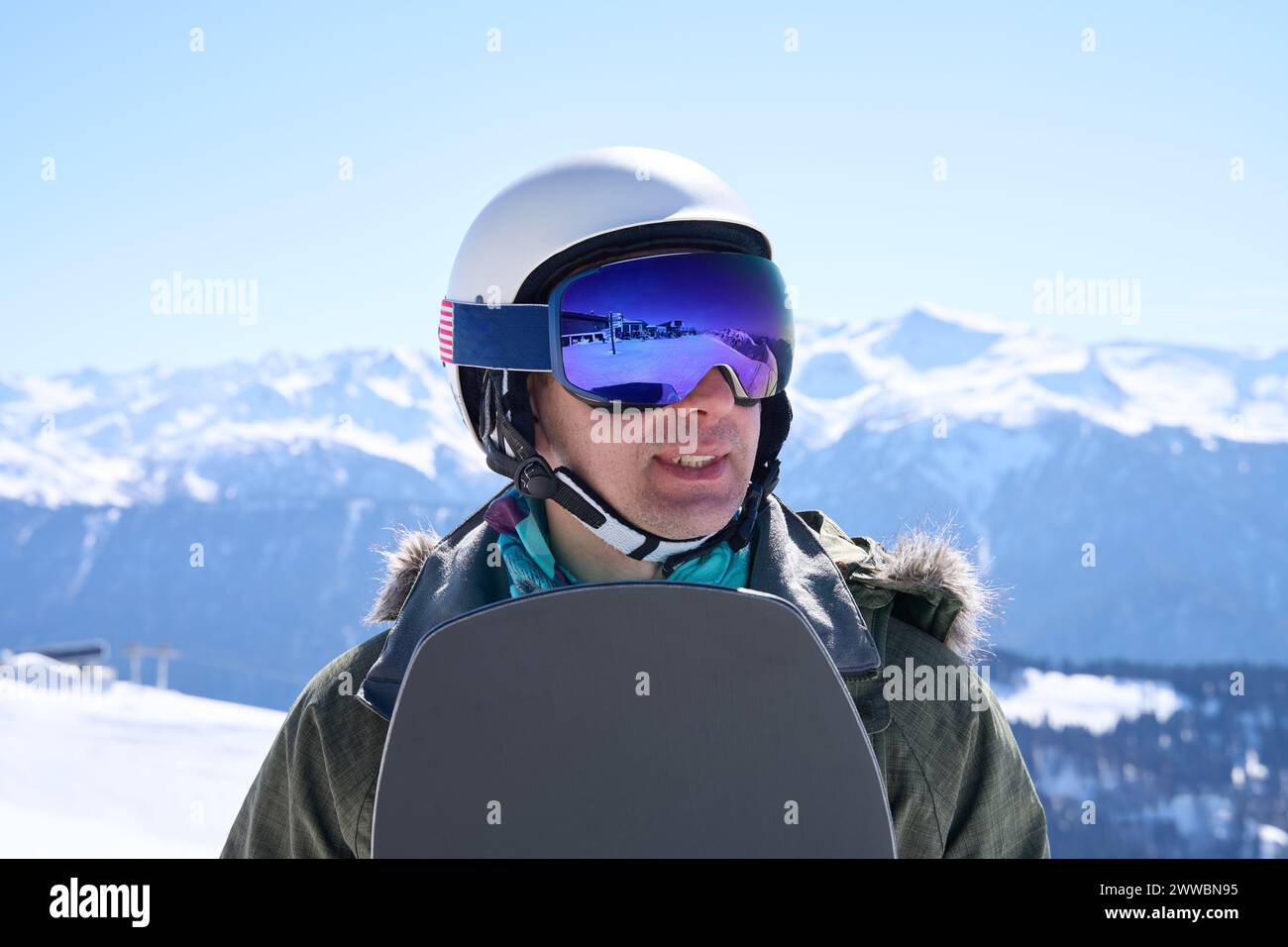 Uno snowboarder rifrangente, vestito di equipaggiamento invernale, si ferma per ammirare il vasto orizzonte alpino, circondato dalla tranquillità delle montagne innevate. Foto Stock