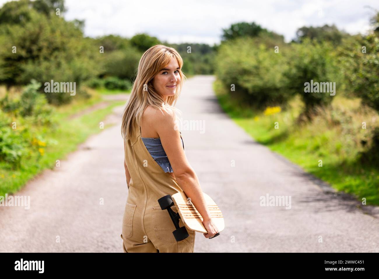 Donna sorridente con skateboard che cammina su strada Foto Stock