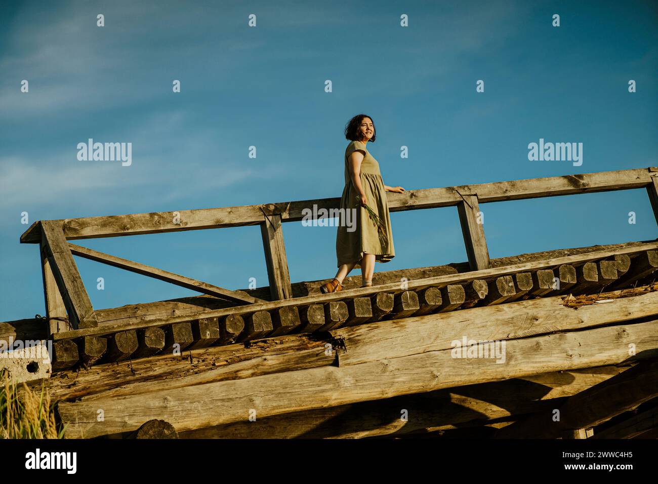 Donna matura spensierata che cammina su un ponte sotto il cielo blu Foto Stock
