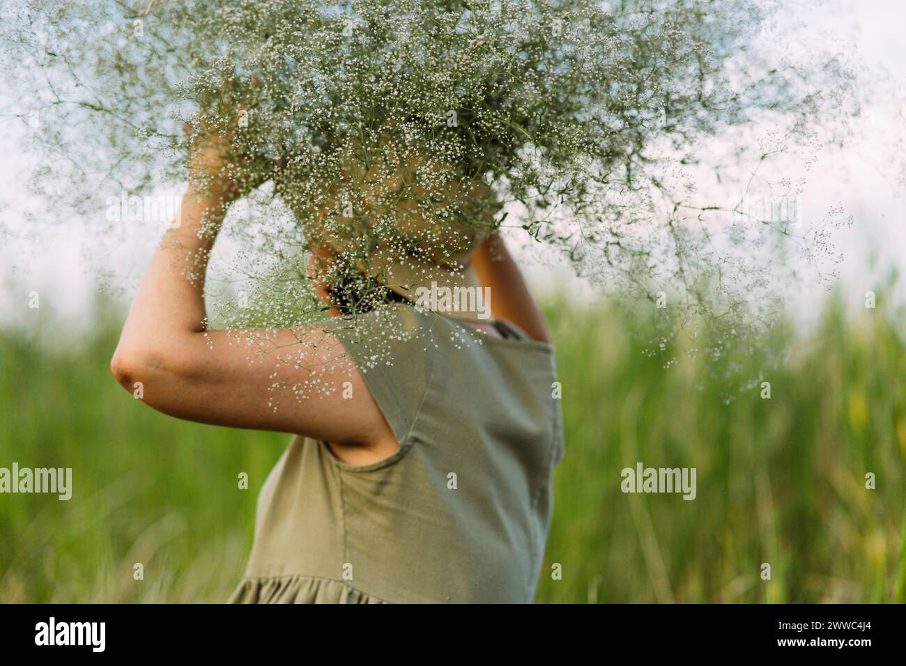 Donna matura che tiene i fiori di gypsophila sulla testa nel campo Foto Stock