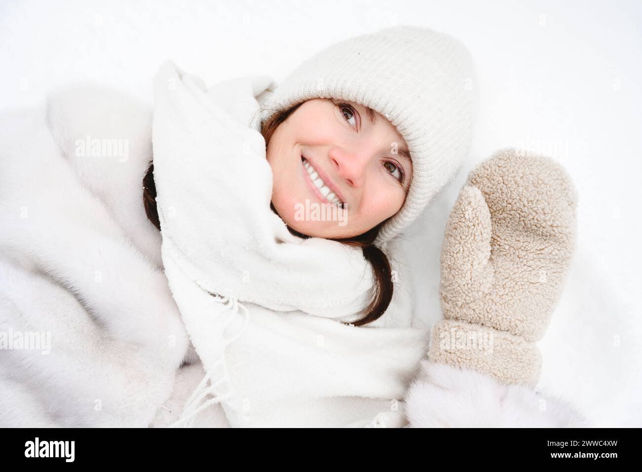 Donna sorridente sdraiata sulla neve in abiti caldi Foto Stock