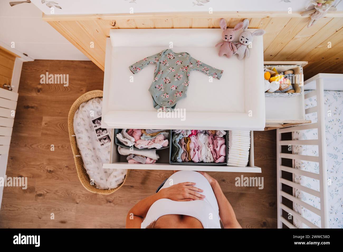 Donna incinta in piedi vicino a vestiti per bambini a casa Foto Stock