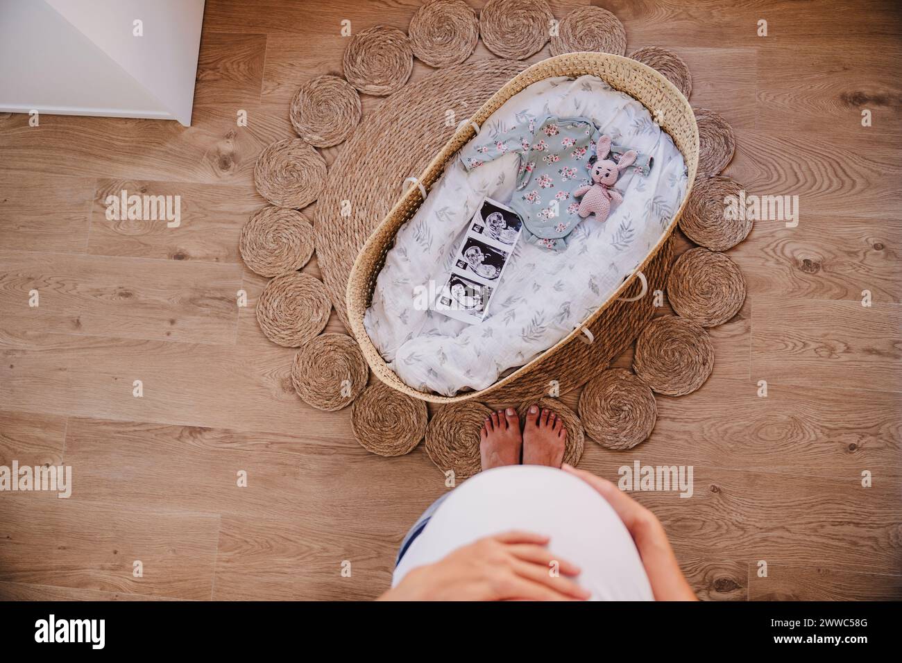 Donna incinta in piedi vicino moses cesto su tappeto a casa Foto Stock