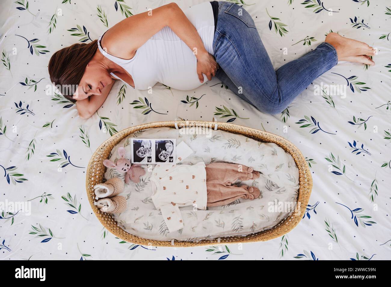 Donna incinta sdraiata vicino a moses cesto a letto a casa Foto Stock